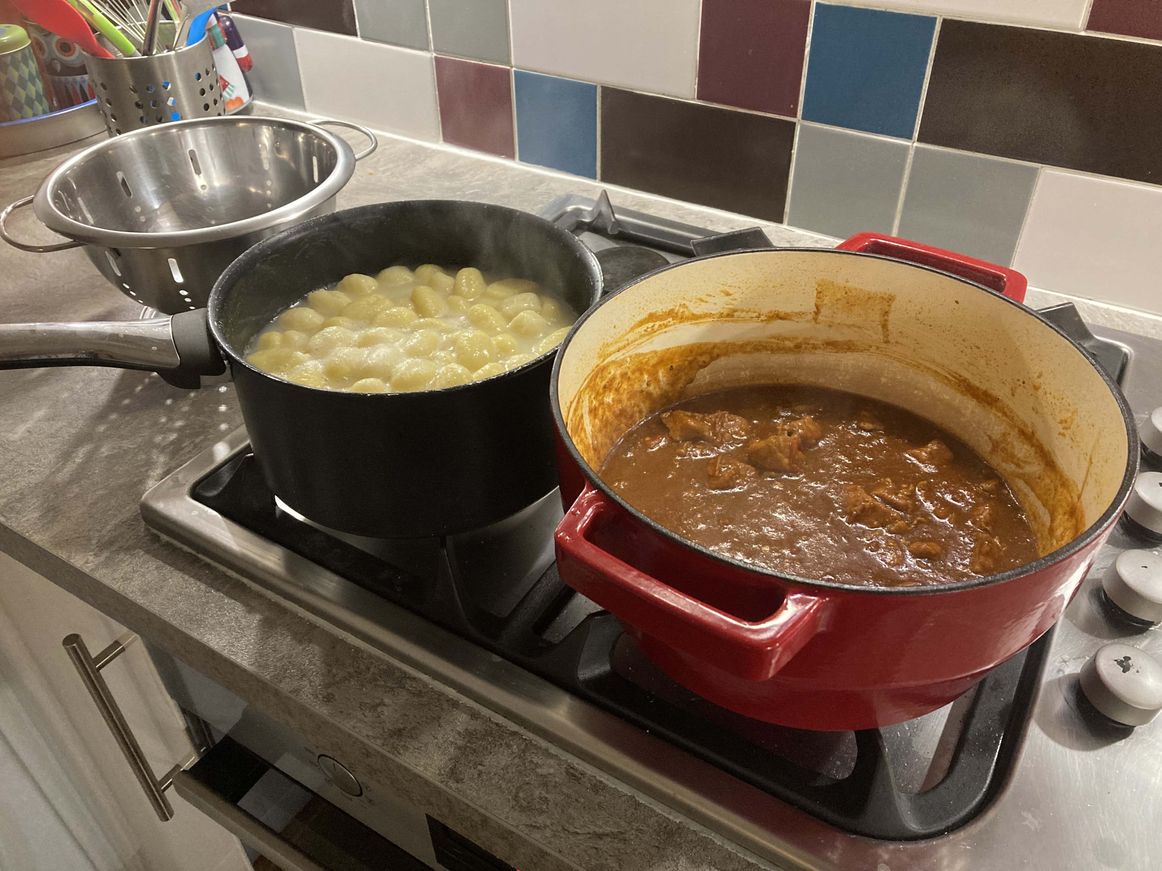 Goulash in a big red dutch oven with some gnocchi cooking in a pot next to it
